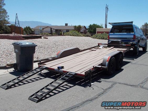 Blue Ford pickup truck with camper shell loaded onto a trailer, seen from the rear