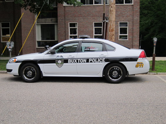 White police car with black stripe and "BUXTON POLICE" text, parked on asphalt