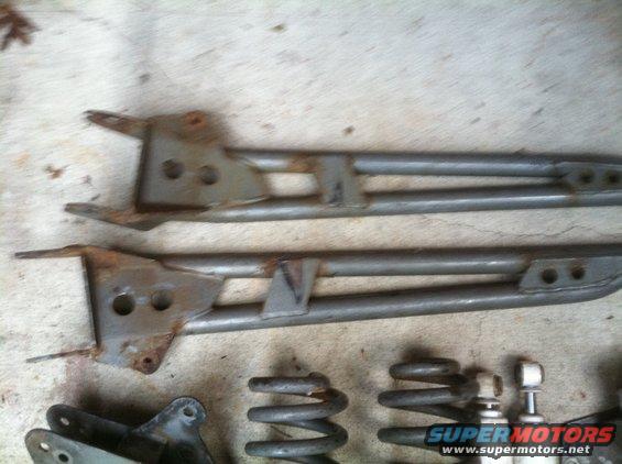 Two rusty metal suspension arms and some coil springs on a concrete surface