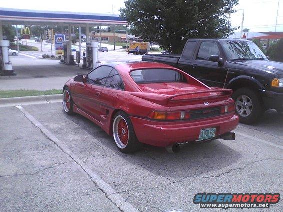 Red Toyota MR2 parked next to a black Ford Ranger pickup truck at a gas station