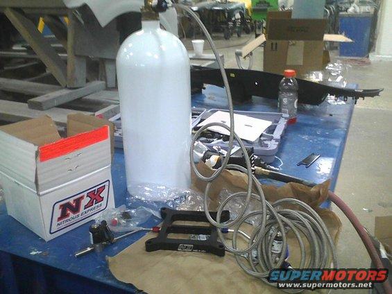 White nitrous oxide tank with braided hose and NX Nitrous Express box on a blue table