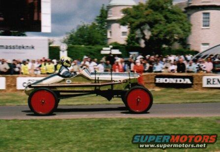 1909 Ford Model T speedster with red wheels and a driver in a helmet