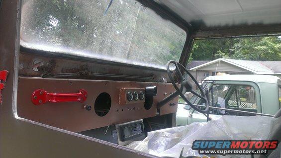 Interior view with red grab handle, three gauges, and steering wheel. Another vehicle visible outside