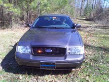 Dark gray 2004 Ford Crown Victoria with a black grille and a blue line sticker on the front