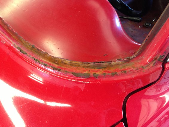 Close-up of rusted metal seam on red car bodywork, showing peeling paint and corrosion