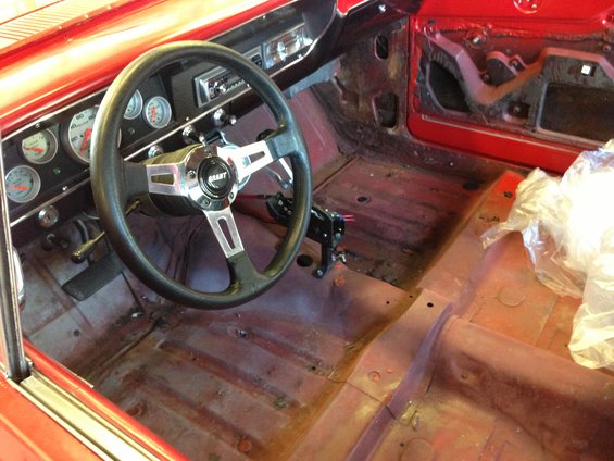 Red car interior with Grant steering wheel, aftermarket gauges, and bare floor panels
