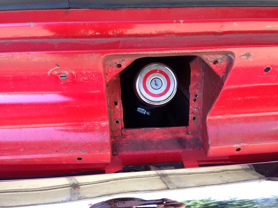 Red vehicle's fuel filler door is open, showing the cap with red and silver rings and a keyhole