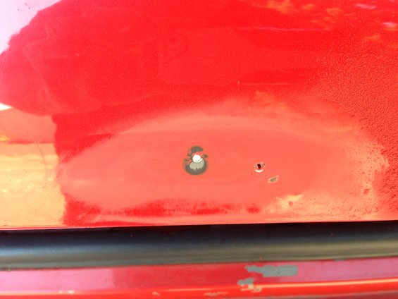 Close-up of a red car panel showing two holes, one larger with a circular gray surround