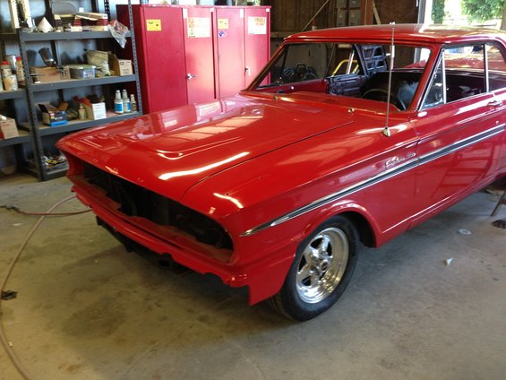 Red 1964 Ford Fairlane coupe with chrome trim and racing wheels, front end removed, in a garage