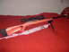 1990 Max II - A rifle with a scope and bipod is displayed on a red surface, accompanied by a pink camouflage sling.