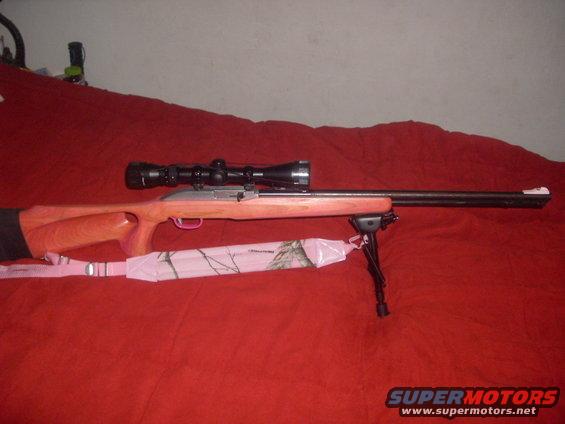 Rifle with wooden stock, black scope, and bipod on a red surface