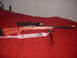 1990 Max II - A rifle with a scope and bipod is displayed on a red surface.