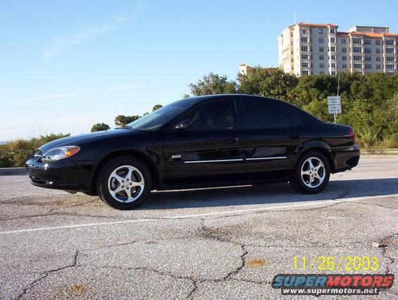 Black 2003 Ford Taurus sedan parked on cracked asphalt, side view