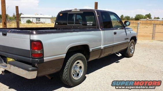 Two-tone brown and silver Dodge Ram pickup truck, rear quarter view, parked on gravel