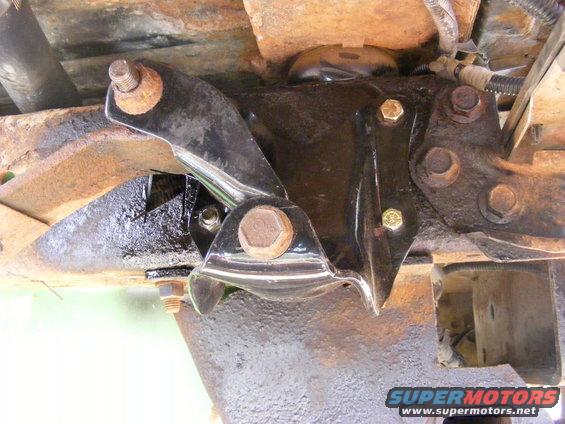 Undercarriage of a vehicle with rusty frame and black metal bracket with bolts