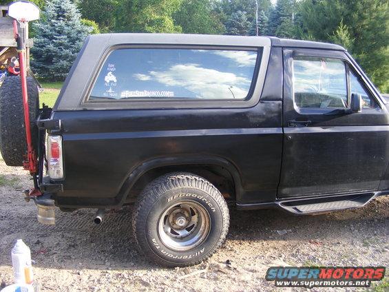 Black Ford Bronco with spare tire on back, side view. Has a sticker on the rear window