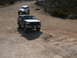 1988 Ford Bronco - Two off-road vehicles, a Ford Bronco and a white Jeep, navigate a dusty trail in a dry, hilly landscape.