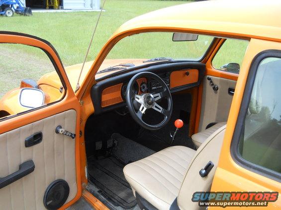 Orange Volkswagen Beetle interior with tan seats, aftermarket steering wheel, and orange shift knob. Visible door panel and dashboard