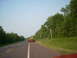 2000 Chevrolet Tahoe - Construction equipment on a trailer travels down a highway lined with trees.