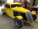 1975 Ford Ranchero - A bright yellow hot rod coupe sits in a garage with two people in the background.
