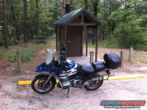 Blue and white BMW motorcycle with black luggage parked near a wooden outhouse