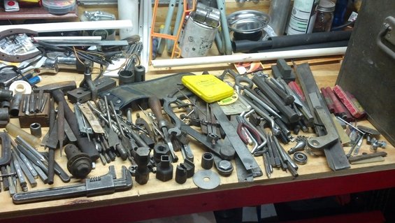 Workbench cluttered with various tools including wrenches, pliers, hammers, and drill bits
