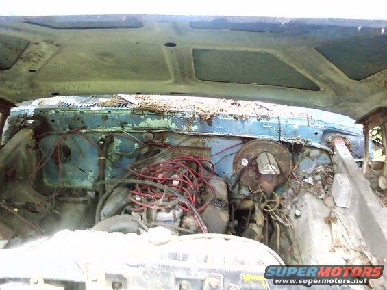 engine bay of a blue car with exposed wiring and rust
