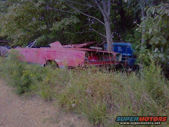 red convertible in weeds, blue truck behind it