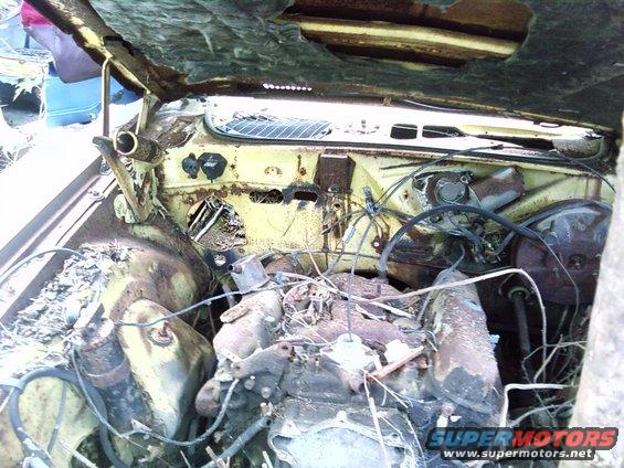 Rusty yellow car engine bay with exposed engine and wiring