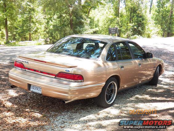 Gold 1993 Ford Crown Victoria parked on gravel near trees, with a camping area sign in the background