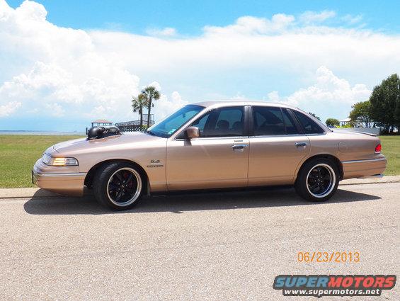 1993 Ford Crown Victoria with hood scoop and custom wheels, parked by the water