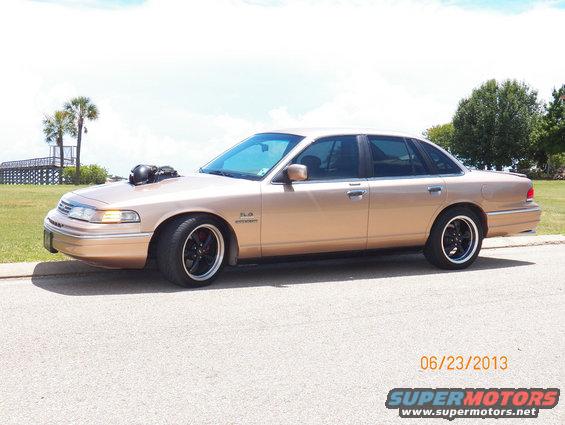 Tan 1993 Ford Crown Victoria with a hood scoop and black rims parked on a street