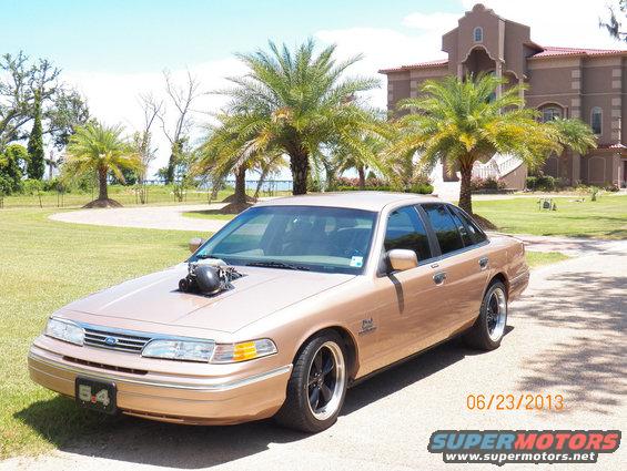Gold 1993 Ford Crown Victoria with a hood scoop and custom wheels parked in front of a large house