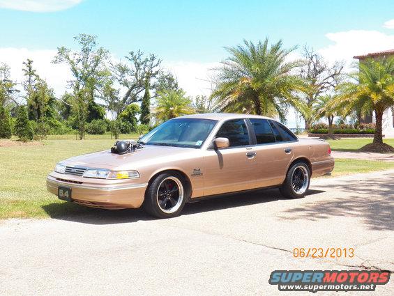 Gold sedan with hood scoop, black rims, and custom exhaust pipes, parked on a paved surface