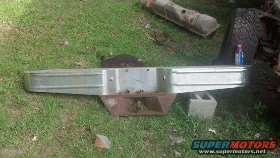 Chrome truck bumper with a rusty hitch receiver, resting on grass and cinder blocks