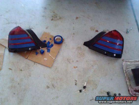 Two car tail lights with blue and red stripes, tape, and some screws on a concrete floor
