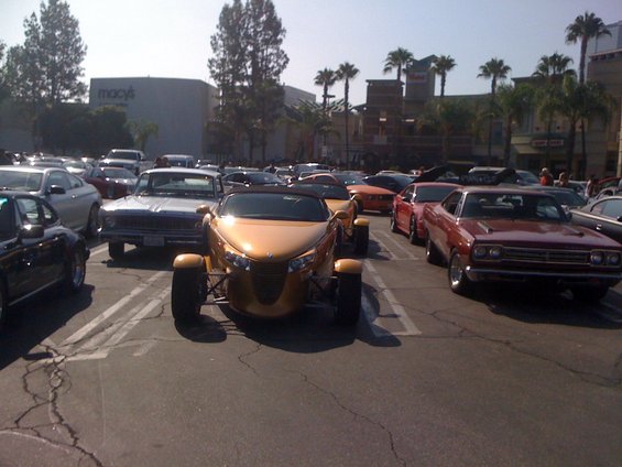 Gold Prowler parked in a lot with other cars, Macy's building in background