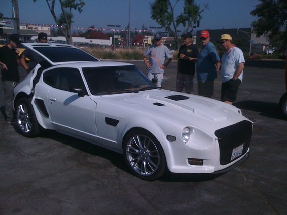 white sports car with custom body kit and aftermarket wheels, people standing around it