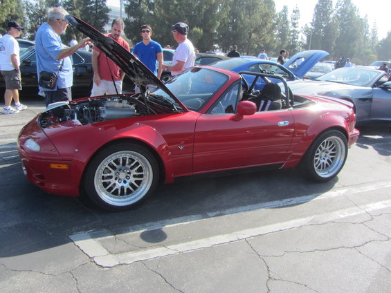 Red convertible sports car with hood open, aftermarket wheels, and wide body kit