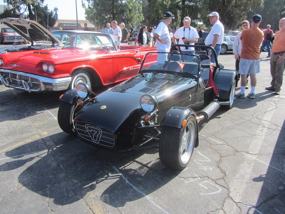 Black sports car with a '7' emblem on the grille, parked next to a red convertible