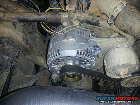 Alternator with a drive belt, hoses, and wiring in an engine bay