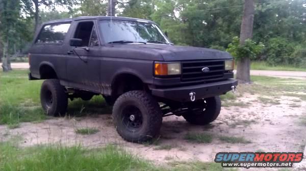 1990 Ford Bronco with aftermarket bumper and lift kit parked on dirt and grass