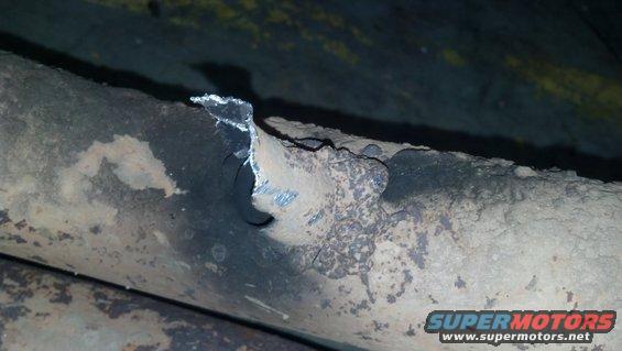 Close-up of a rusted exhaust pipe showing a hole and damage
