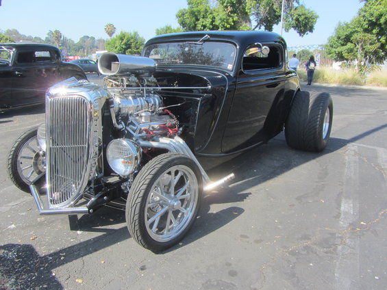 black hot rod coupe with a big chrome blower sticking out of the hood, parked next to another dark car