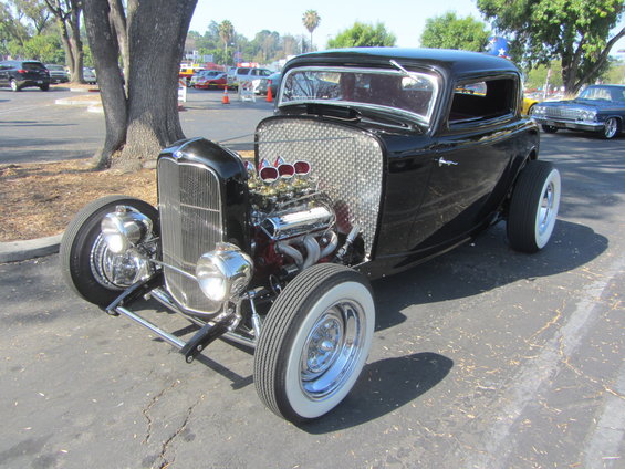 Black hot rod with exposed engine, chrome grille, and whitewall tires