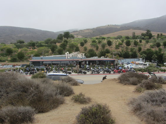 Motorcycles parked outside Neptune's Net restaurant with hills in background