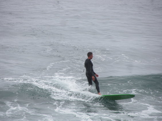 Man in wetsuit surfing on a green surfboard in choppy water
