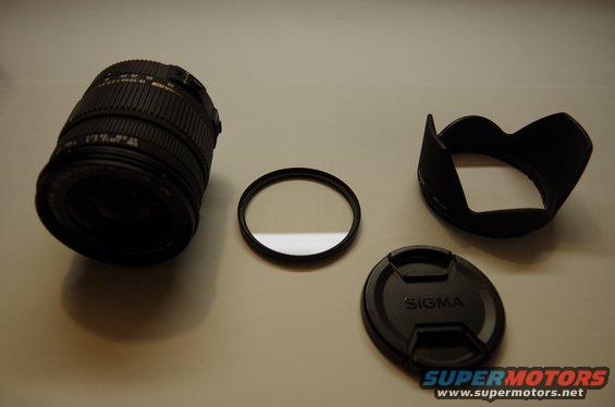 Camera lens, filter, lens hood, and lens cap laid out on a surface. The lens cap has 'SIGMA' on it
