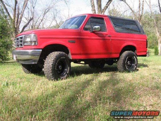 Red 1992 Ford Bronco, lifted, with black off-road tires, parked on grass