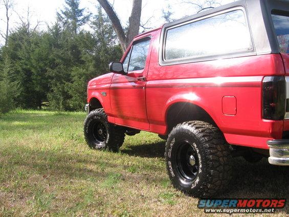 Red 1992 Ford Bronco with lifted suspension and off-road tires parked on grass